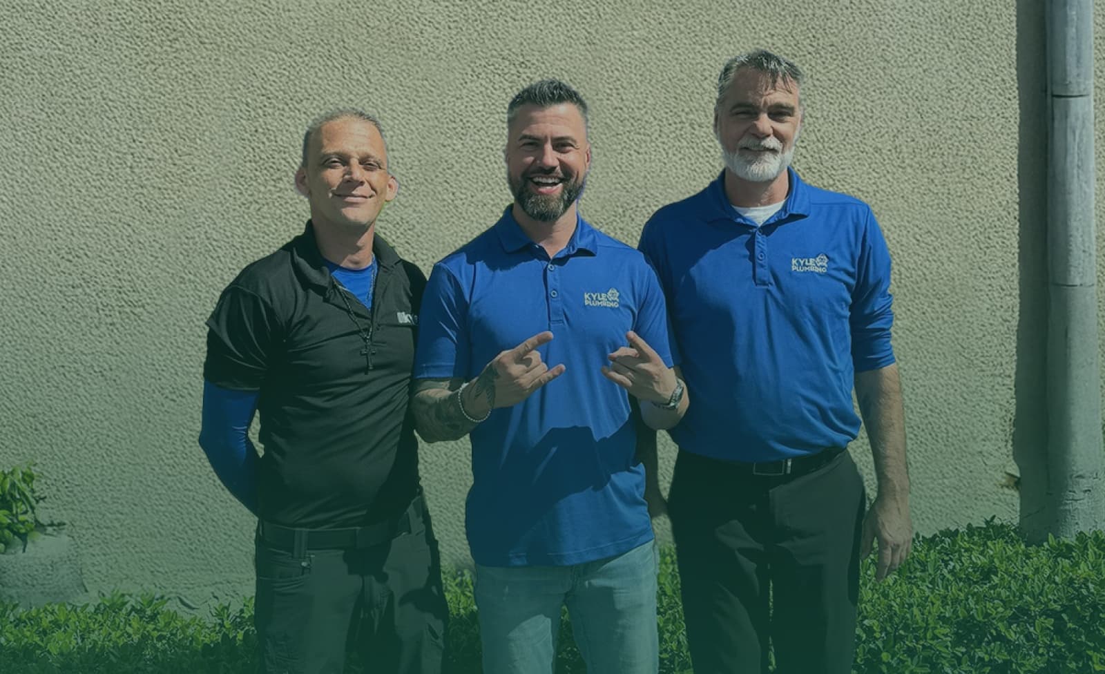 Three plumbers in blue uniforms working on plumbing